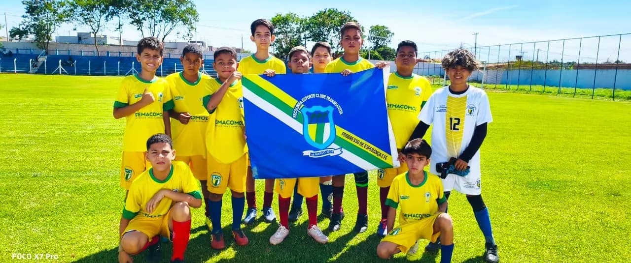 Equipe de amarelo segurando a bandeira do clube no gramado