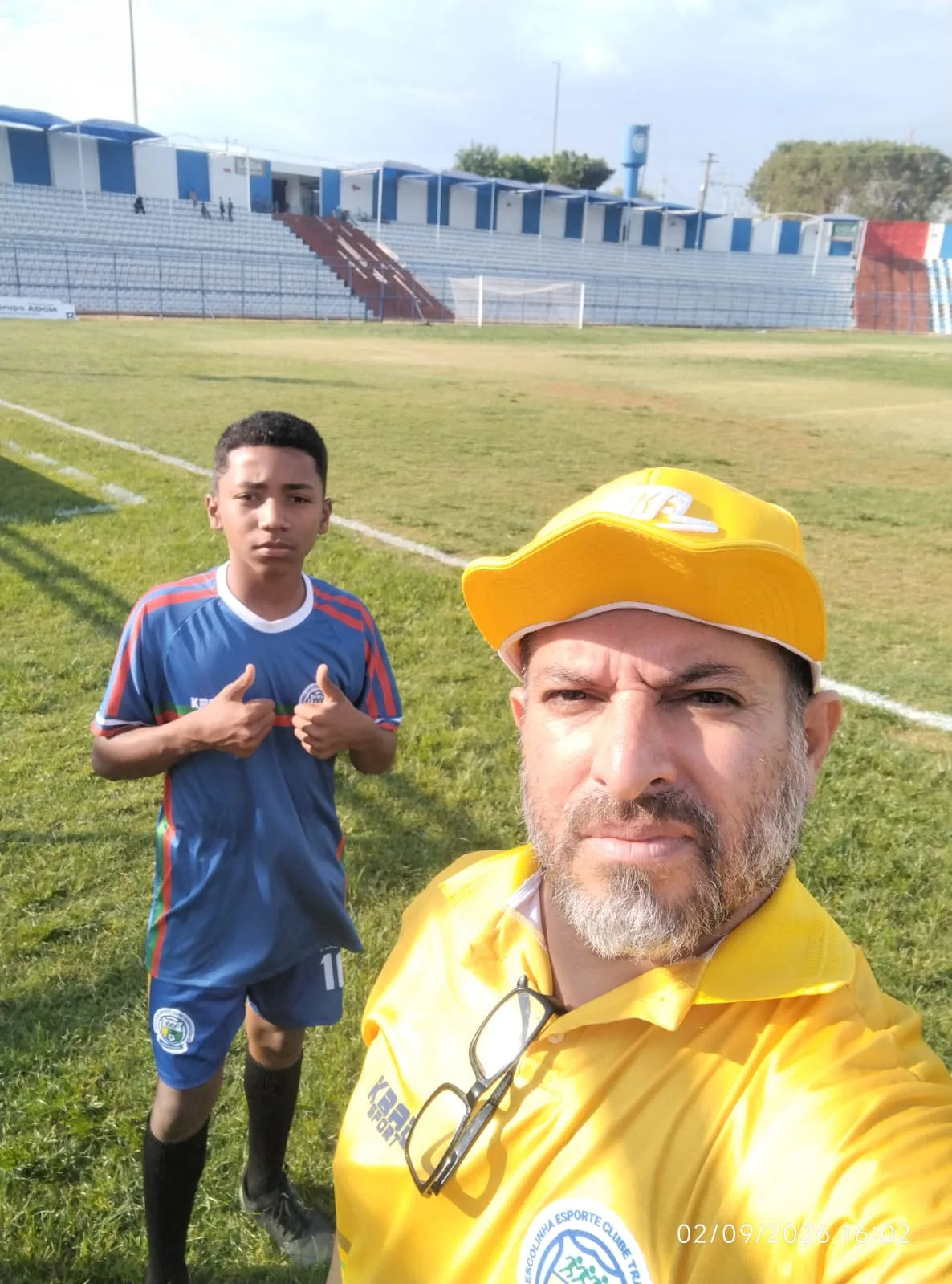 Treinador de boné amarelo com um atleta no gramado do estádio